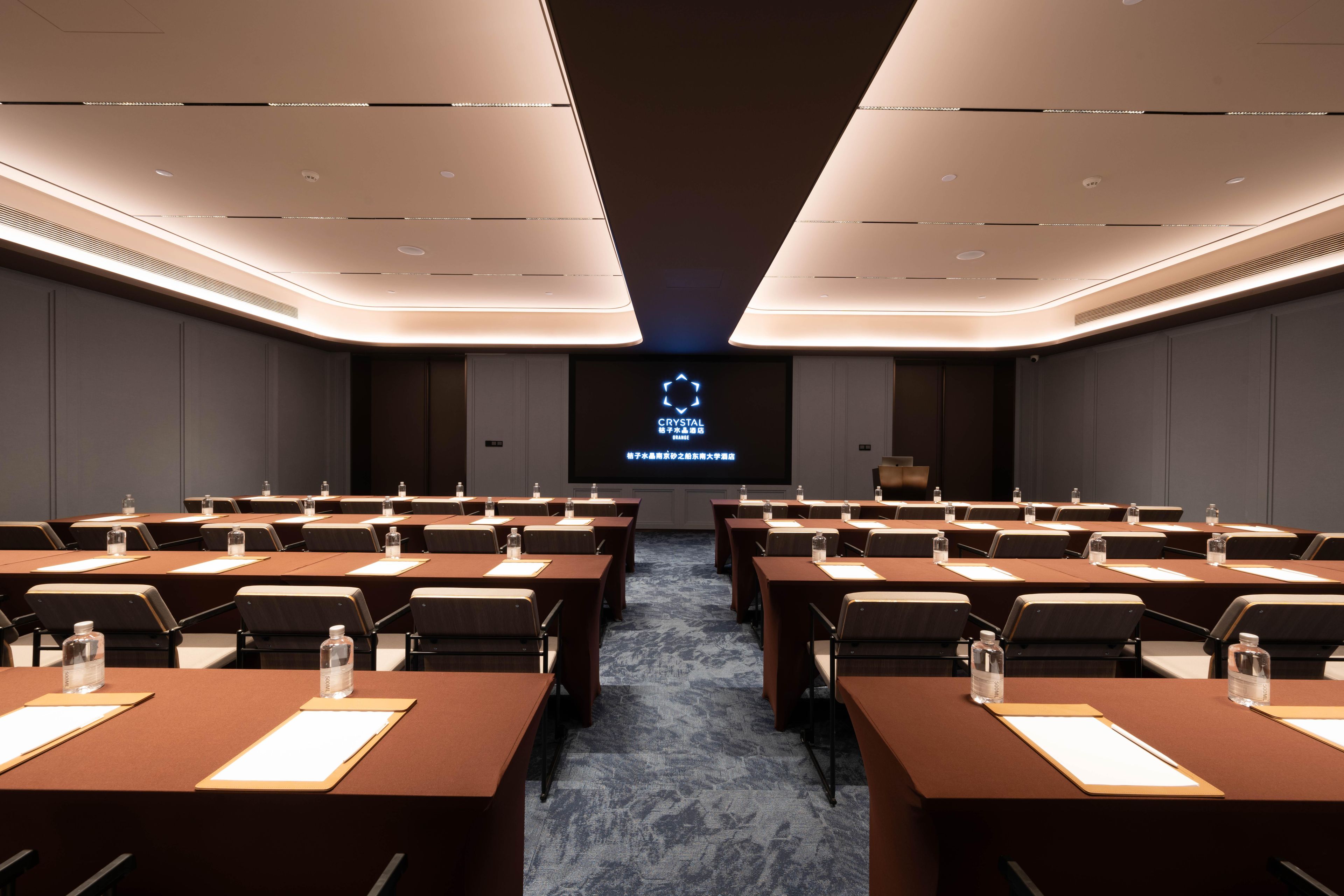 A conference room with multiple tables and chairs, a large screen at the front, and a modern ceiling design.