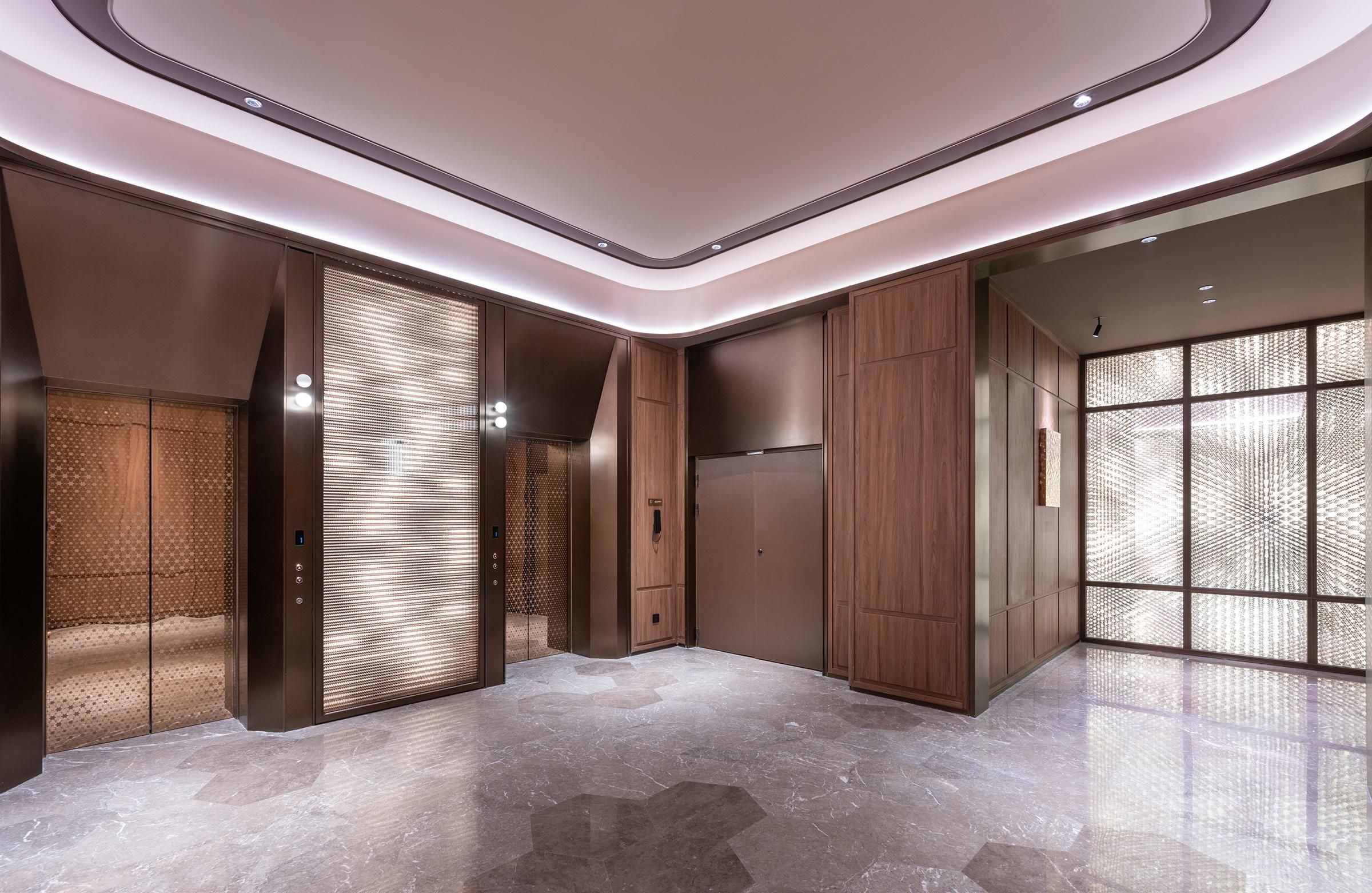 Un ascensor moderno con detalles metálicos, pared revestida de madera y suelo de mármol.