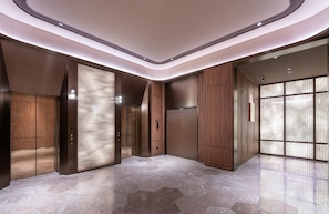 Un ascensor moderno con detalles metálicos, pared revestida de madera y suelo de mármol.