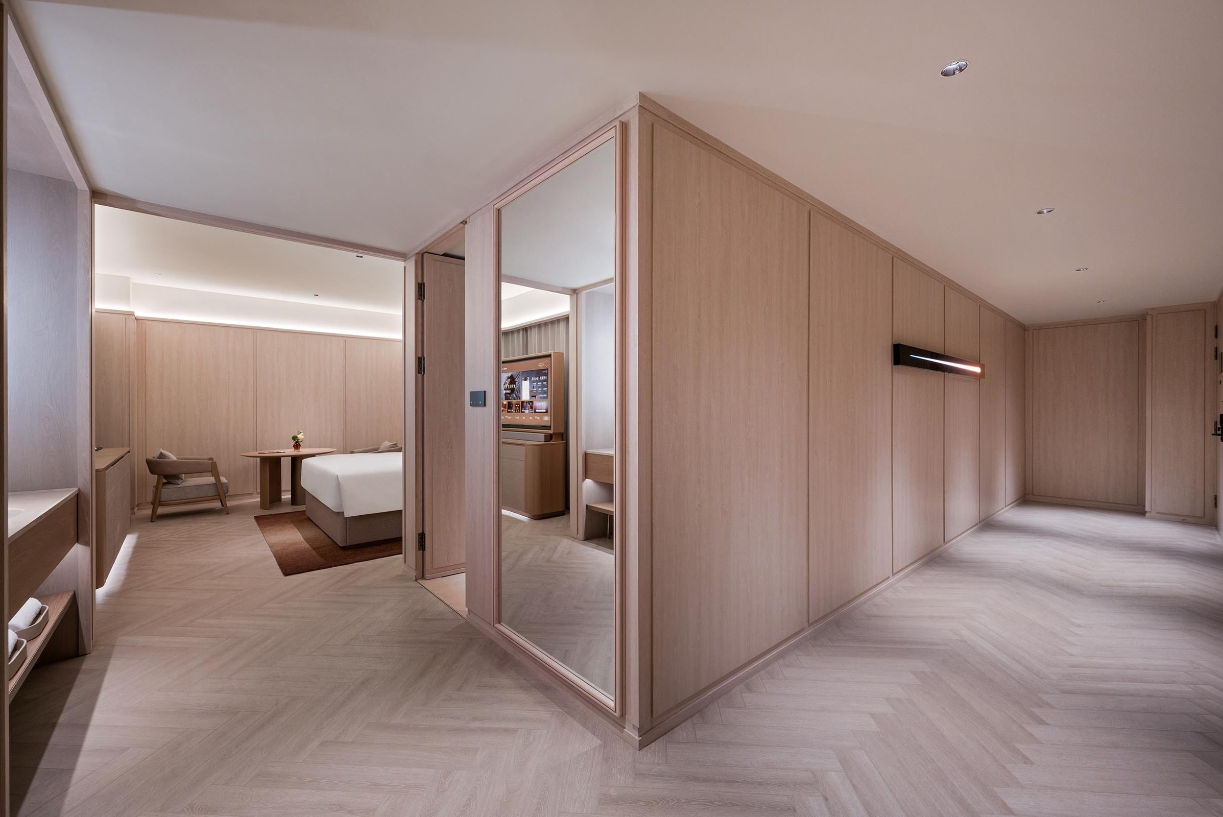 A modern hotel room with a large mirror, a bed, a desk, and a wardrobe.