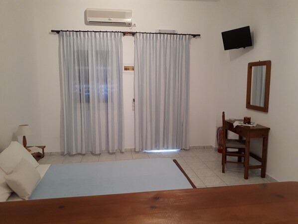 Una habitación con cama, escritorio, silla, televisor y aire acondicionado.