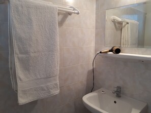 A bathroom with a white towel hanging on a towel rack, a hairdryer on a counter, and a sink with a mirror above it. - Hotel Paradisos Oia (Santorini)