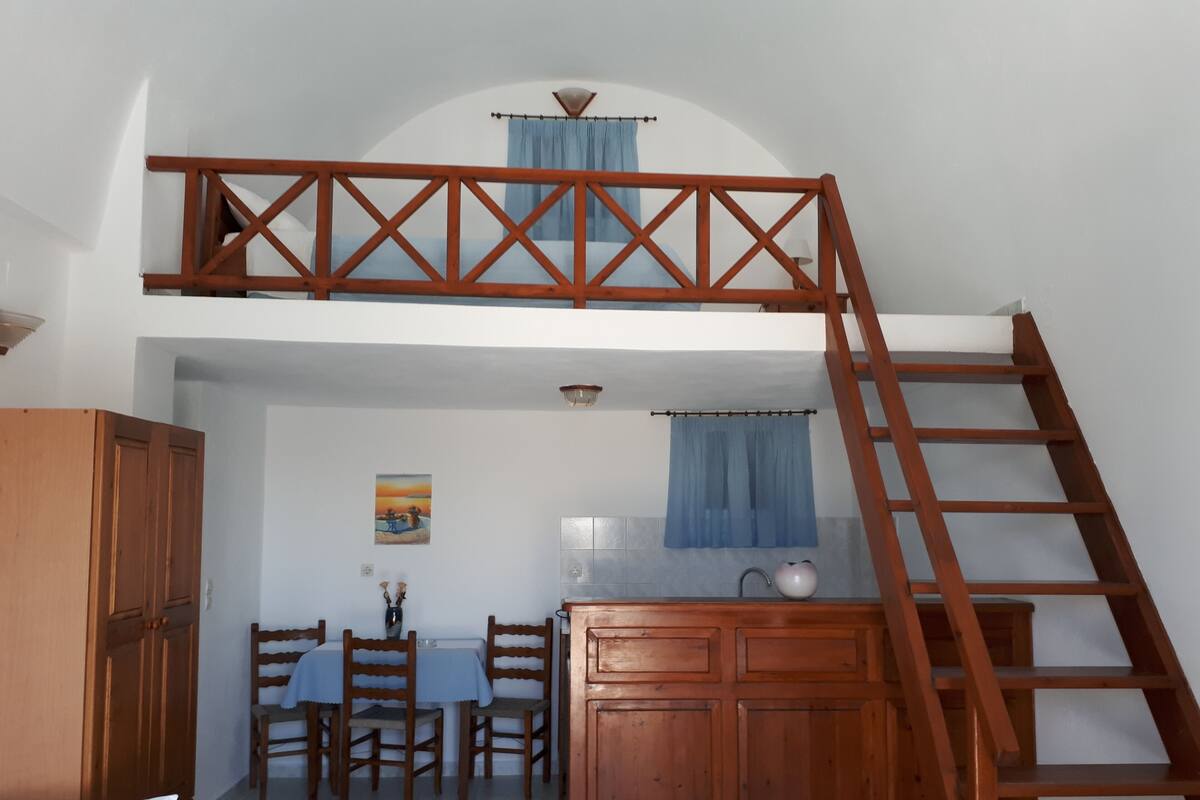 A bedroom with a loft bed, wooden furniture, a dining area, and a bathroom.