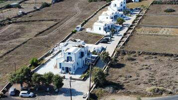 A row of white buildings with a central road, parked cars, and sparse vegetation.
