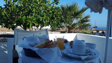A breakfast setup on a balcony with a table, a basket of bread, a glass of orange juice, and a cup.