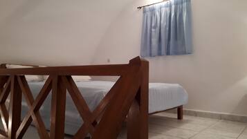 A bedroom with a wooden bed frame, a single bed with a blue bedspread, a window with a blue curtain, and a white wall.