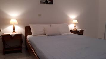 Una cama bien hecha con dos lámparas de noche, una mesita auxiliar pequeña y un cuadro colgado en la pared.