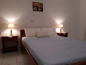 A neatly made bed with two bedside lamps, a small bedside table, and a wall-mounted picture.