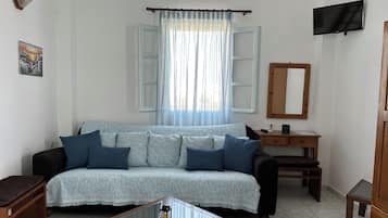 A living room with a sofa, a coffee table, a TV, a desk, and a mirror.