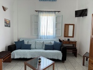 A living room with a sofa, a coffee table, a TV, a desk, and a mirror. - Hotel Paradisos Oia (Santorini)