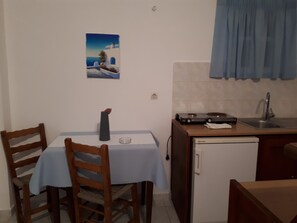 A compact kitchen with a dining table, chairs, a small refrigerator, and a sink. - Hotel Paradisos Oia (Santorini)