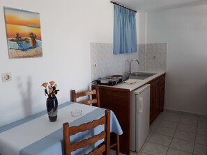 A small kitchen with a dining table, chairs, a sink, and a stove. - Hotel Paradisos Oia (Santorini)