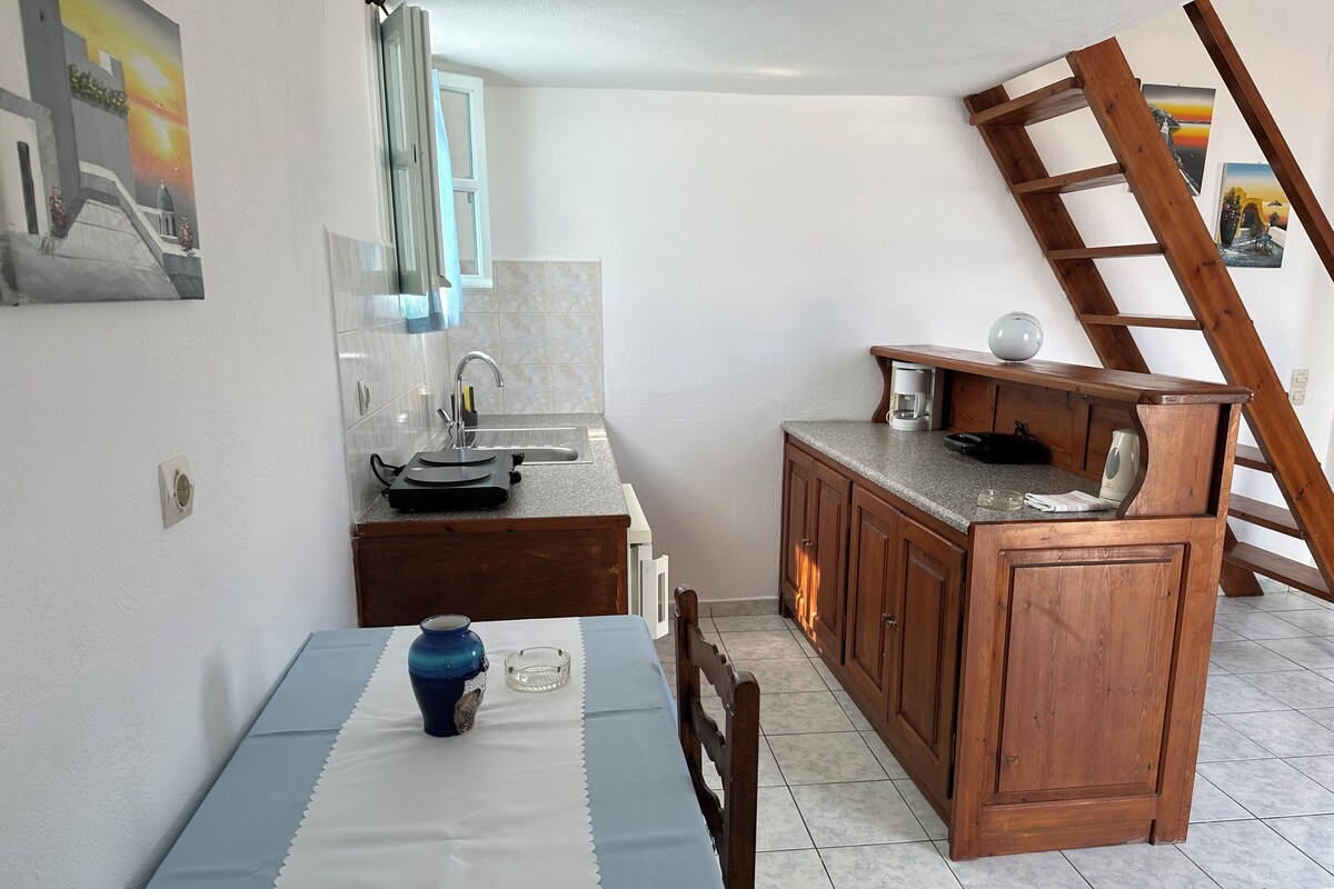 A compact kitchen with a sink, wooden cabinets, a table with a blue tablecloth, and a ladder leaning against the wall.