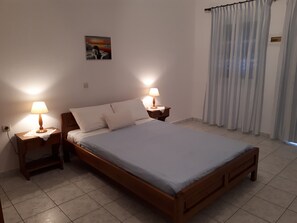 Un dormitorio con una cama de madera, dos mesitas de noche con lámparas, un cuadro en la pared y una ventana con cortinas.
