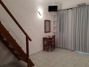 A staircase leading to a room with a dining table and chairs, a television mounted on the wall, and a window with curtains. - Hotel Paradisos Oia (Santorini)