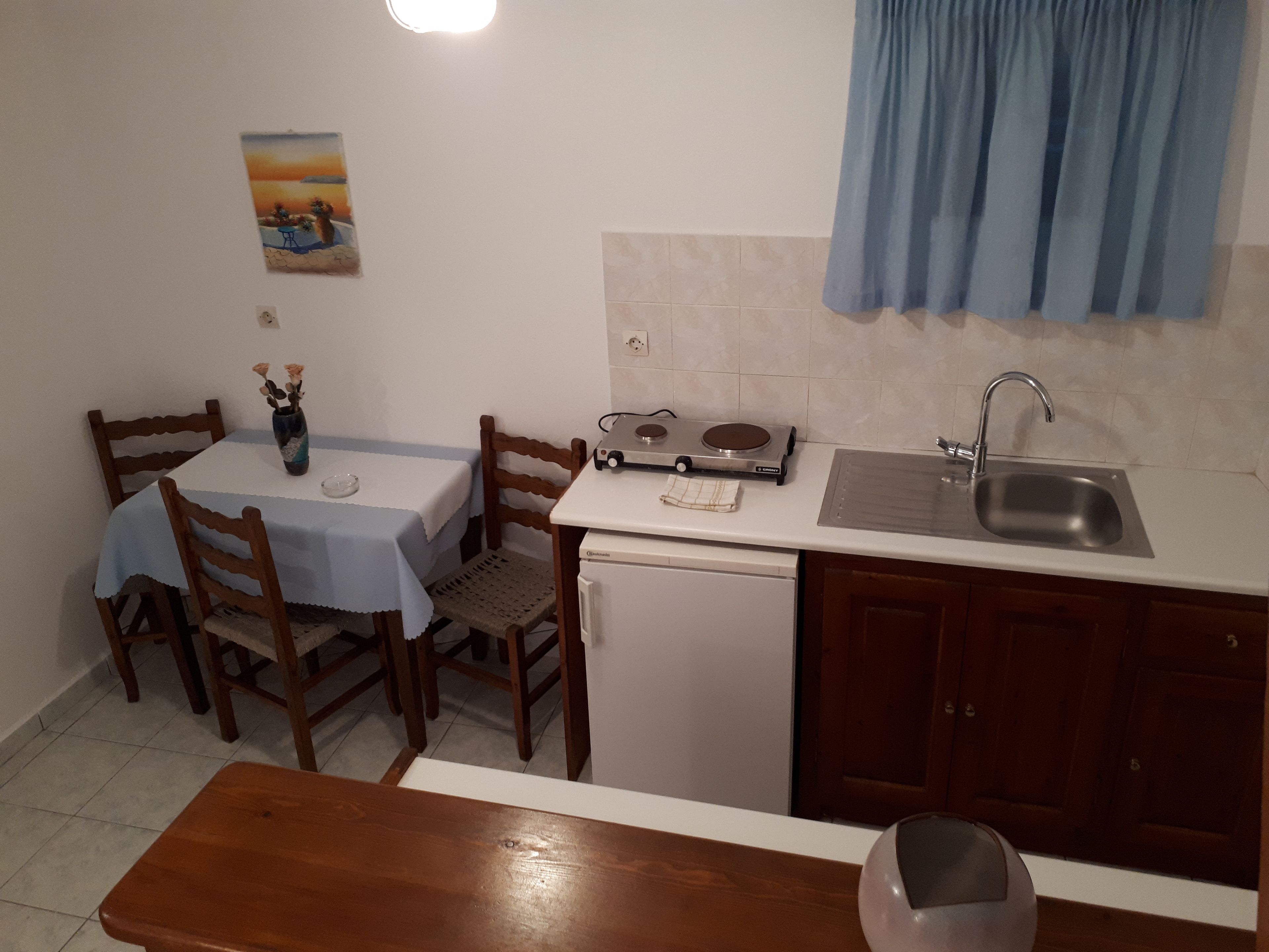 A compact kitchen with a dining table, chairs, a small refrigerator, a sink, and a stove.
