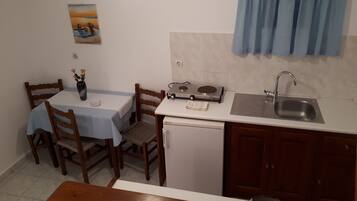 A compact kitchen with a dining table, chairs, a small refrigerator, a sink, and a stove.