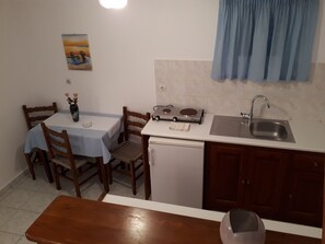 Una cocina compacta con una mesa de comedor, sillas, un refrigerador pequeño, un lavamanos y una estufa.