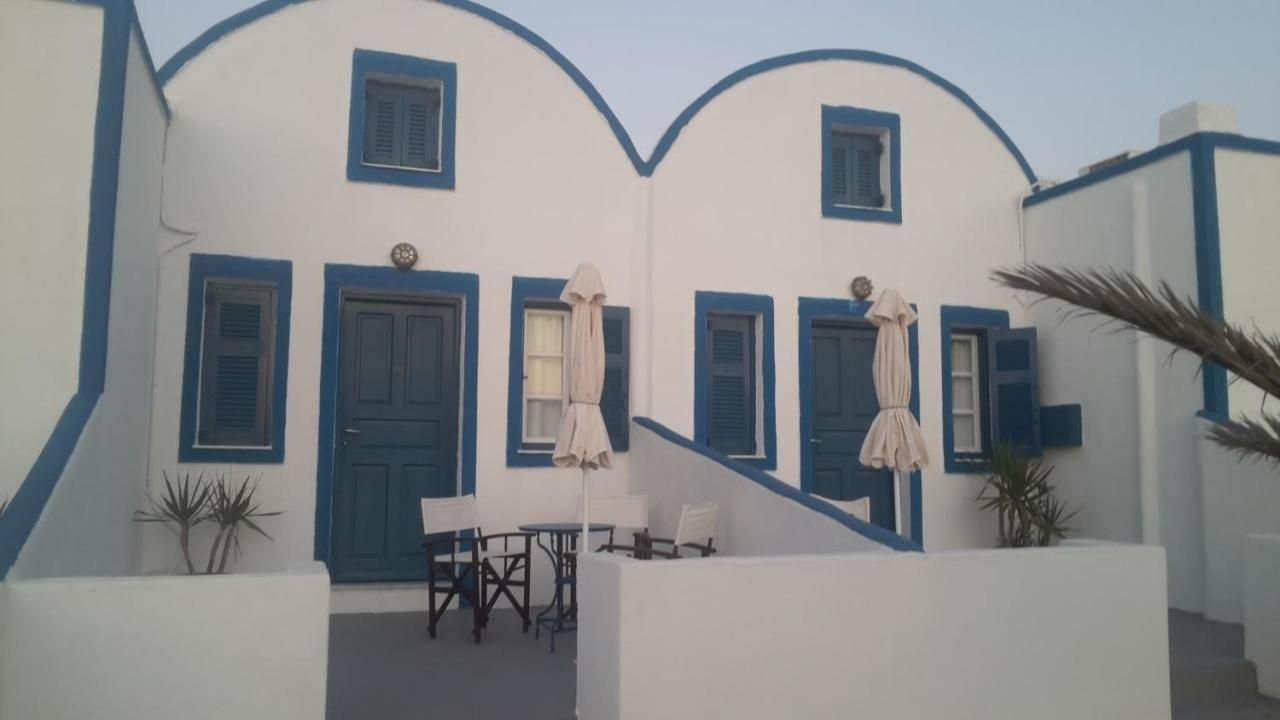 Un edificio blanco con detalles y contraventanas azules, una escalera y mobiliario exterior con sombrillas.