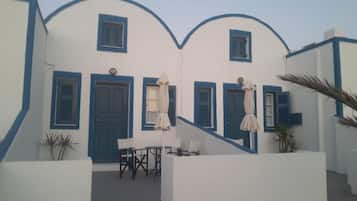 Un edificio blanco con detalles y contraventanas azules, una escalera y mobiliario exterior con sombrillas.