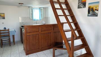 A kitchen with a wooden cabinet, a wooden ladder, a tiled floor, a window with a curtain, and a sink.