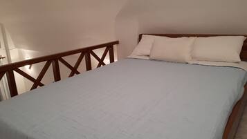 Un dormitorio con cama, cabecera de madera y pared blanca.