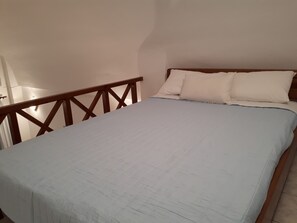 A bedroom with a bed, wooden headboard, and a white wall.