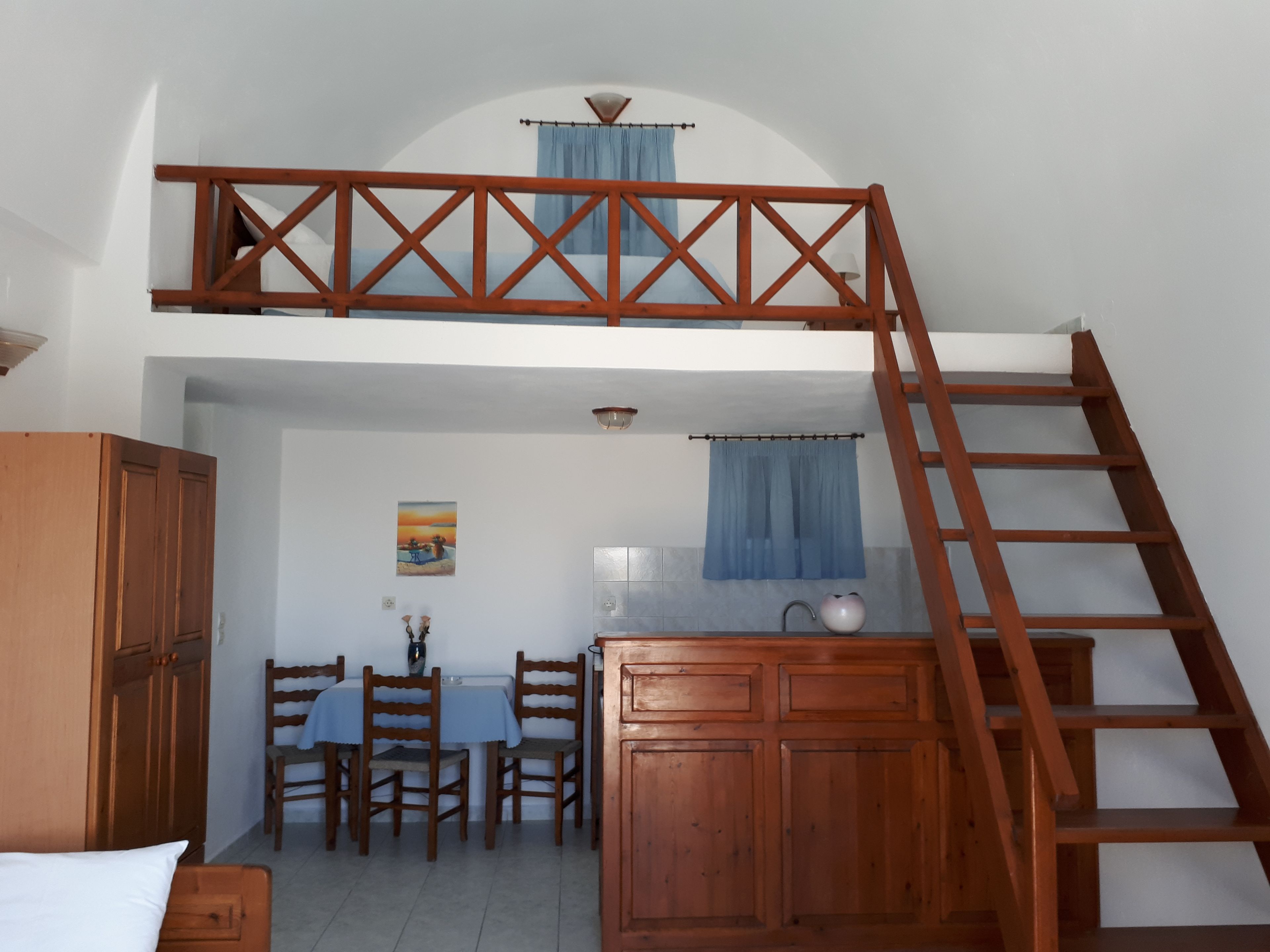 A bedroom with a loft bed, wooden furniture, a dining area, and a bathroom.