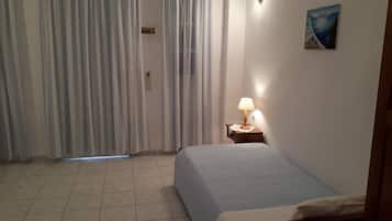 A bedroom with a bed, a nightstand with a lamp, a painting on the wall, and a window with curtains.