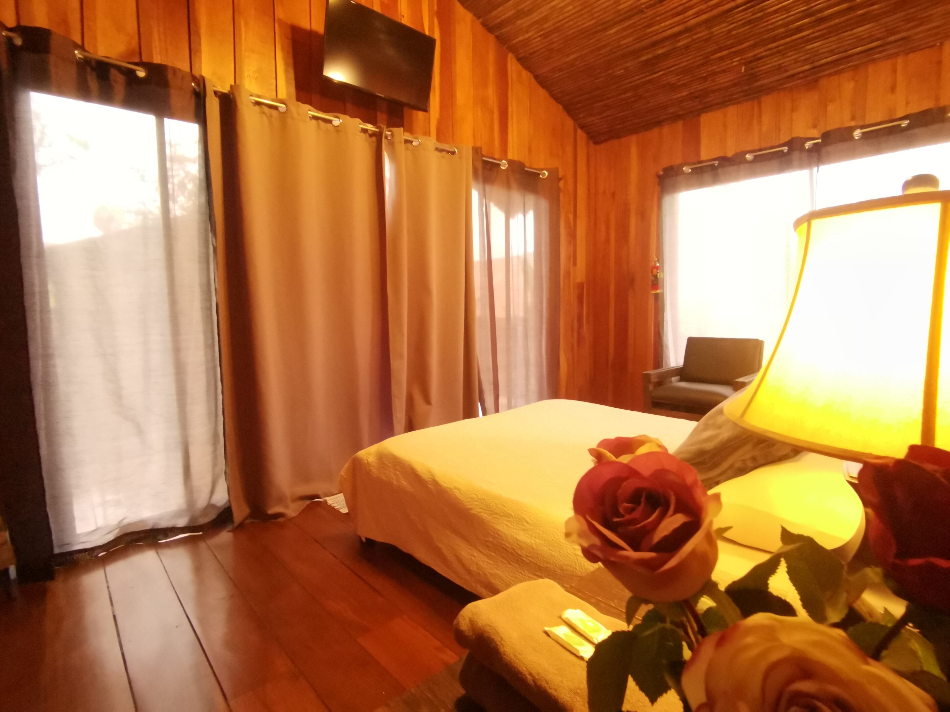 Une pièce en bois avec un lit, des rideaux, une chaise et une lampe.
