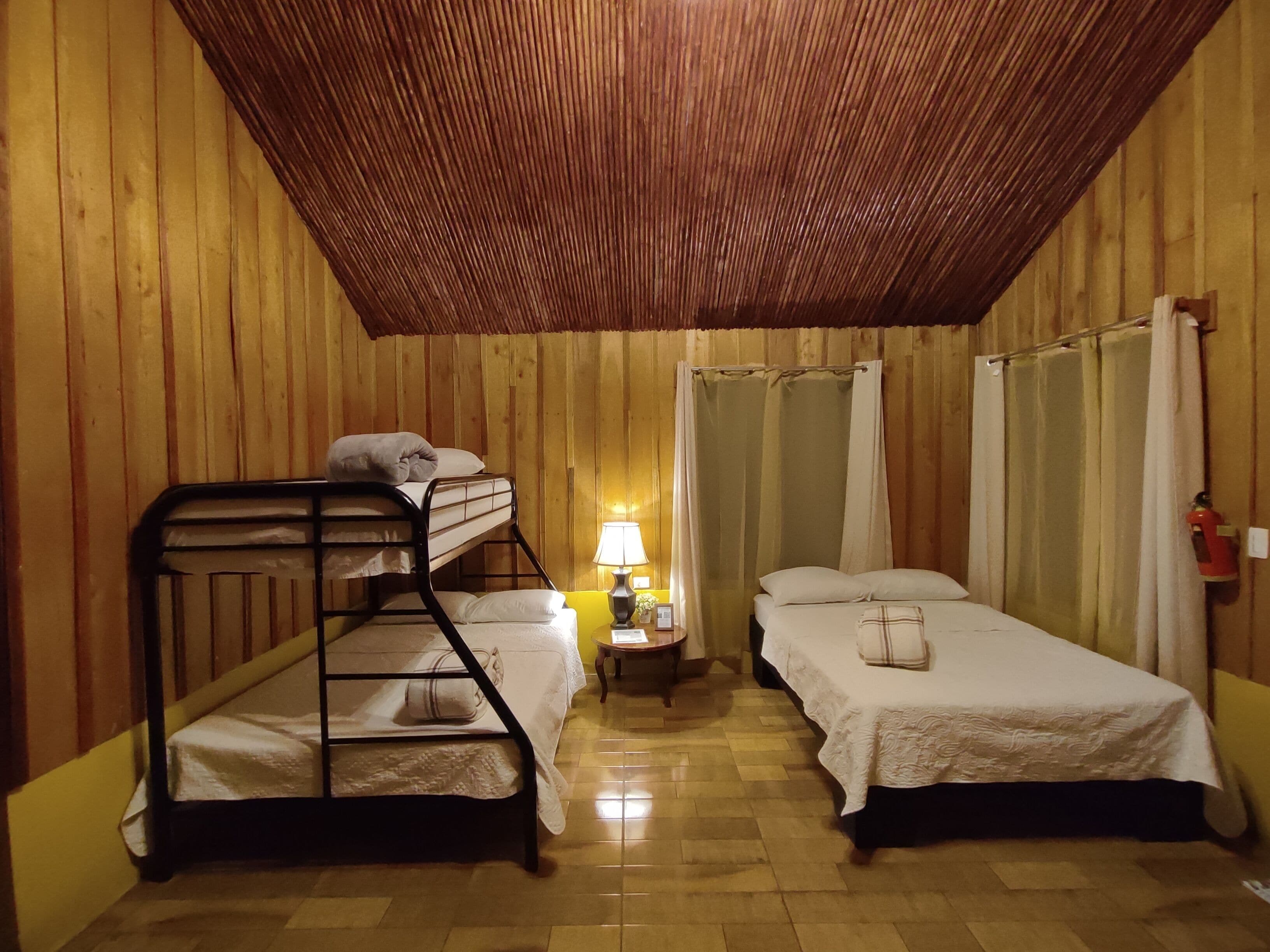 A room with two bunk beds, a small table with a lamp, and a shower curtain.