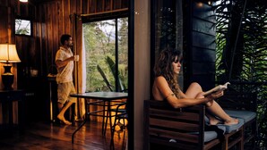 A wooden interior with a person reading a book, another person walking, and a table with a lamp. - Las Cabanas (Venecia)