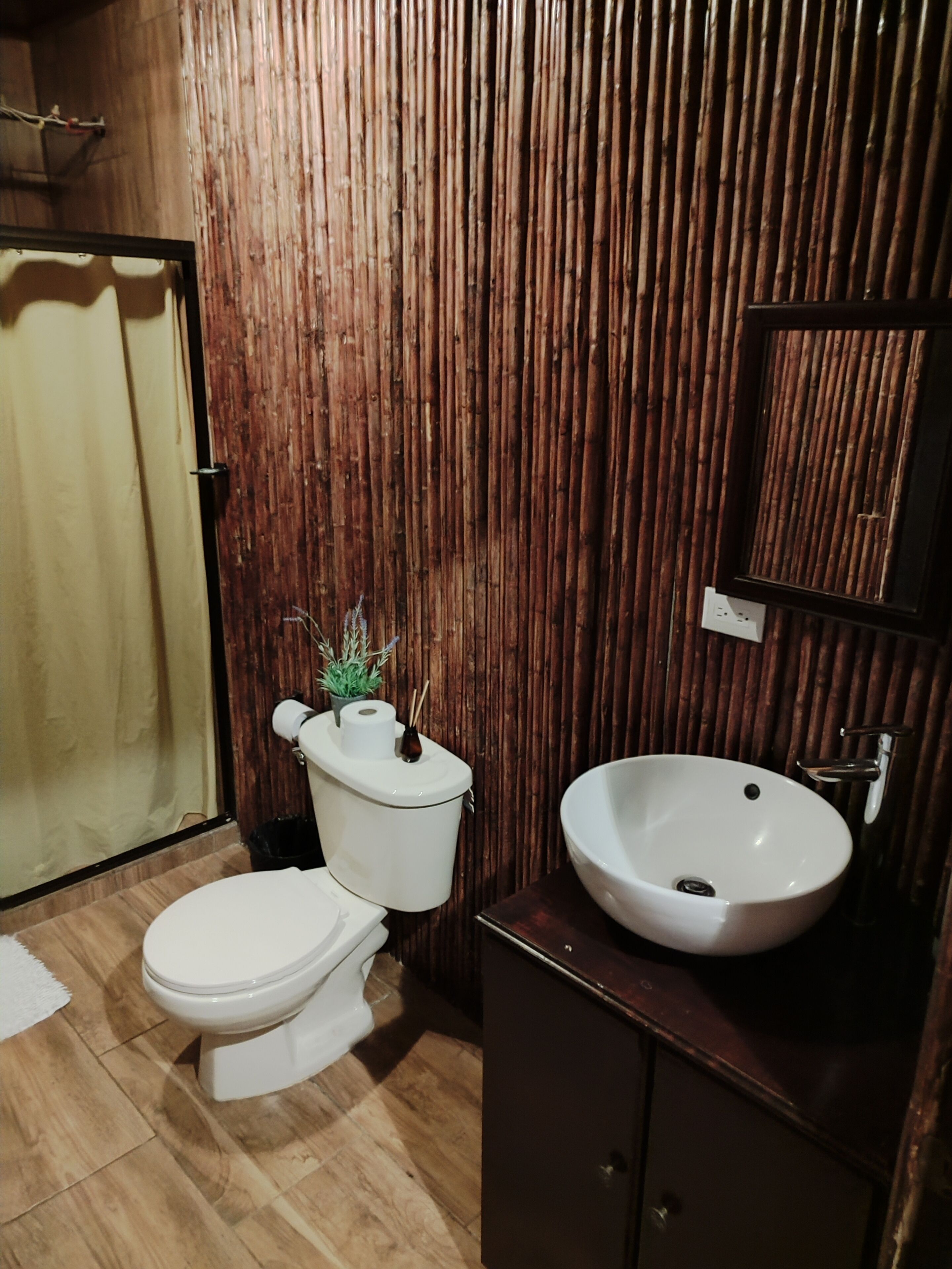 Un baño con pared de madera, inodoro, lavamanos y espejo.