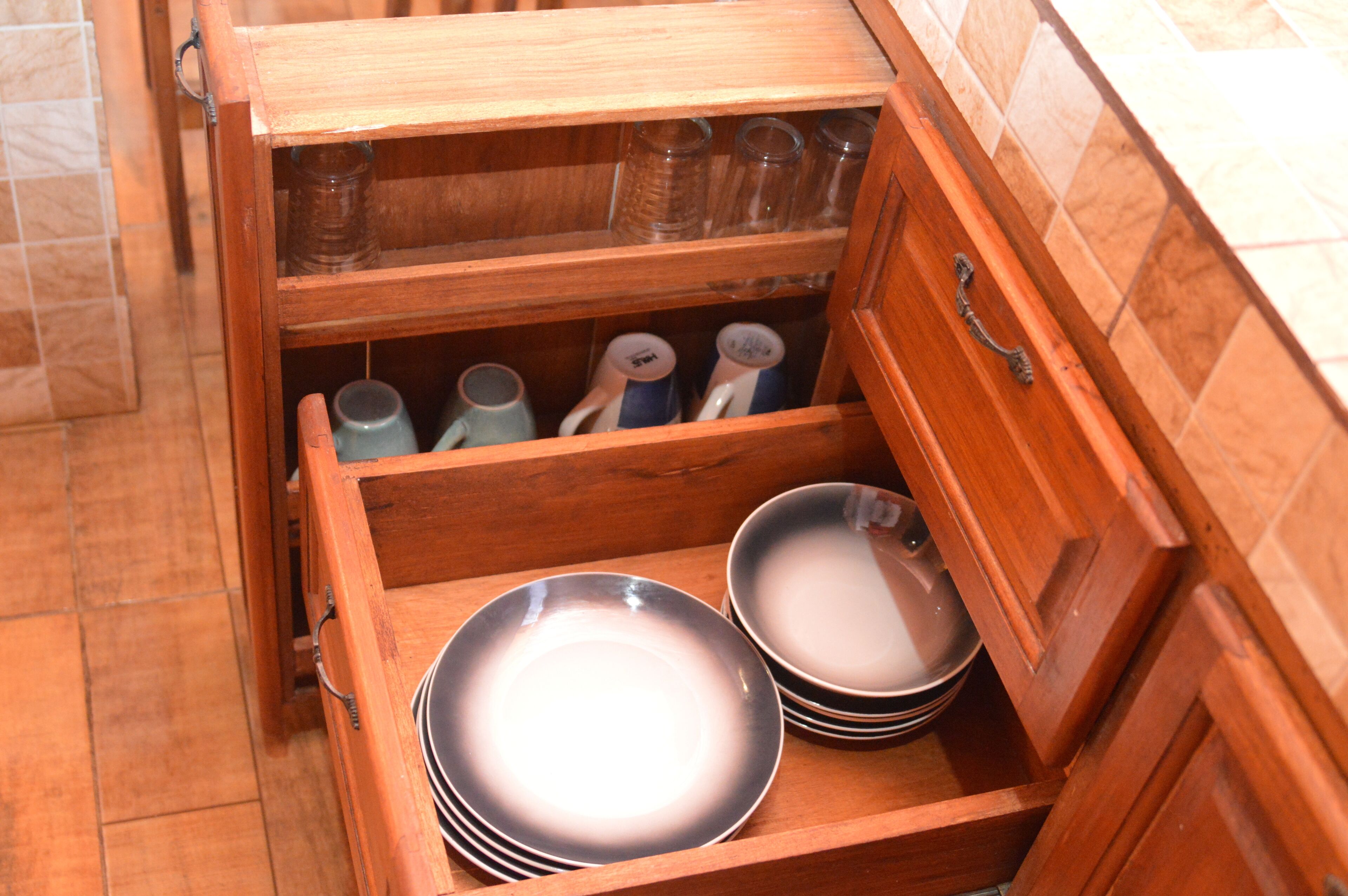 A wooden kitchen cabinet with multiple shelves and drawers, containing various kitchenware items.