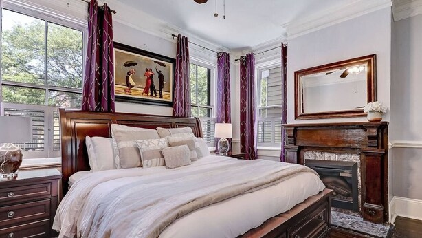 A bedroom with a large bed, a fireplace, a painting, and a view of trees through the window. - Historic Savannah Condo, Sleeps 6, Pool, Dogs Ok (Savannah)