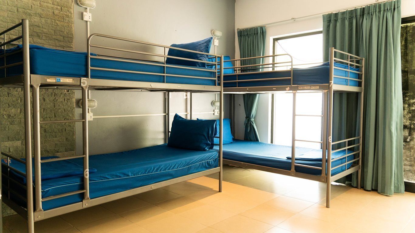 Habitación con literas, dos camas, una ventana con cortinas y pared de ladrillo.