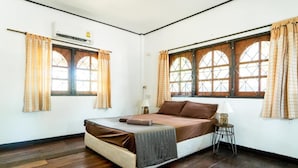 Un dormitorio con una cama, dos ventanas con cortinas, un equipo de aire acondicionado y una mesita de noche con una lámpara.