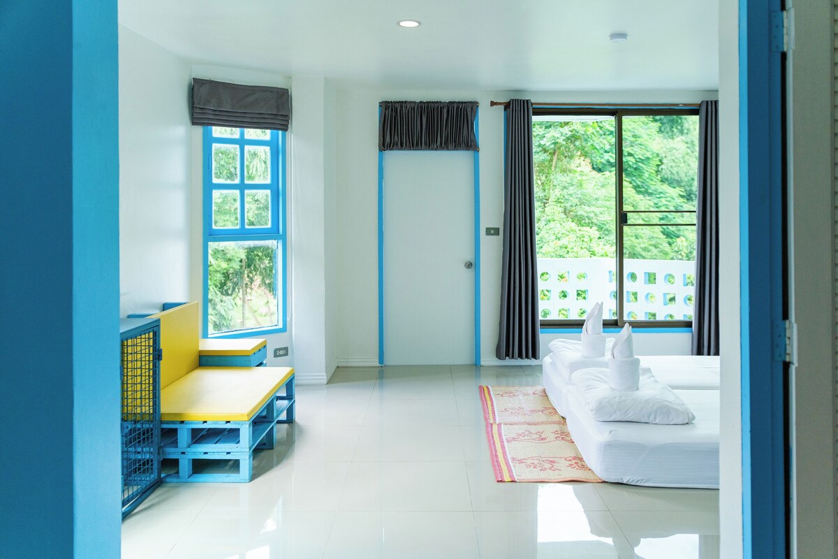 A room with a bed, a window with curtains, a small seating area, and a door.