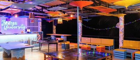 A spacious venue with tables and benches, a neon sign, and hanging umbrellas.