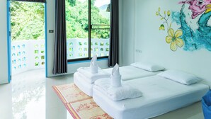 Habitación de hotel con dos camas, un ventanal con cortinas, un mural colorido y vistas al exterior con vegetación.