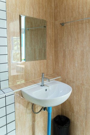 Ein Badezimmer mit einem weißen Waschbecken, einem Spiegel und einer schwarzen Mülltonne.