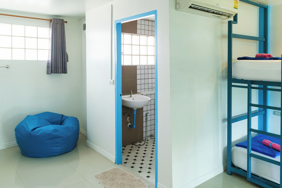 Ein Zimmer mit einem Etagenbett, einem blauen Sitzsack, einem Badezimmer mit Waschbecken und einem Fenster mit Vorhang.