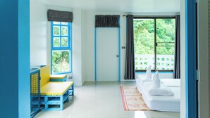 Una habitación con cama, ventana con cortinas, un pequeño rincón de descanso y una puerta.