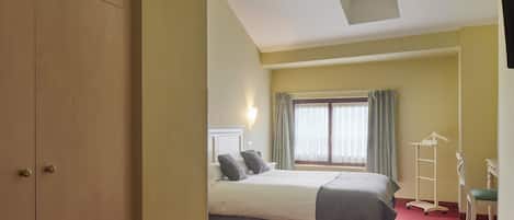 Una habitación de hotel con una cama, un ventanal con cortinas, una mesita de noche y un armario.