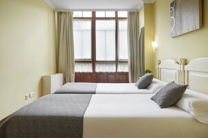 Habitación de hotel con dos camas, una ventana con cortinas, una lámpara en la pared y un radiador.