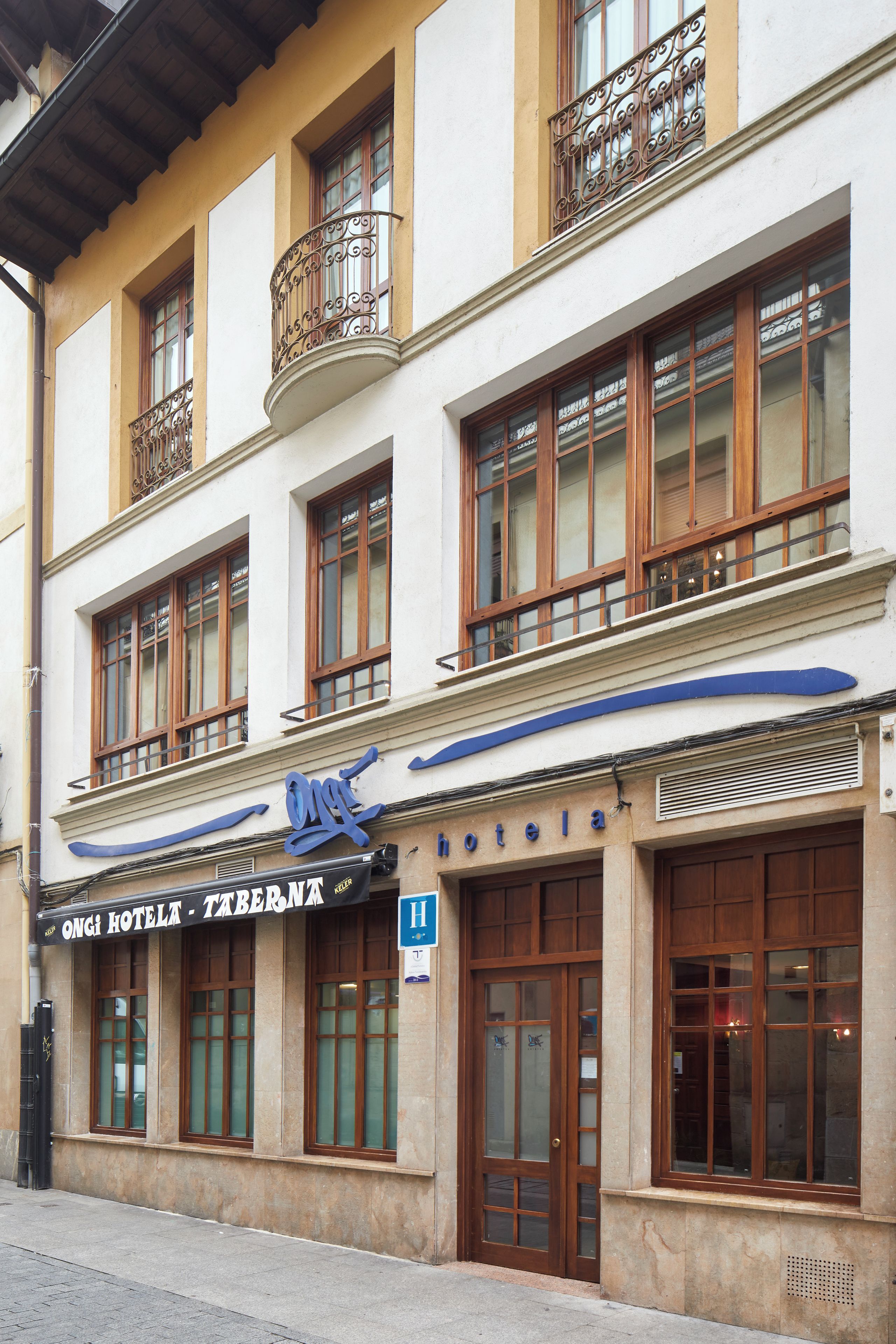 A hotel facade with multiple windows, a balcony with ornate metal railings, and a sign indicating it is a hotel.