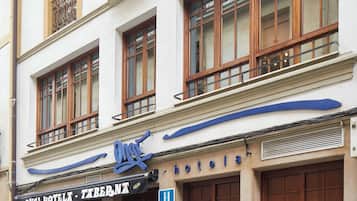 A hotel facade with multiple windows, a balcony with ornate metal railings, and a sign indicating it is a hotel.