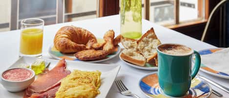 A breakfast table with croissants, toast, scrambled eggs, ham, and a cup of coffee.