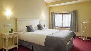 Habitación de hotel con cama, mesitas de noche, cortinas en la ventana y perchero.
