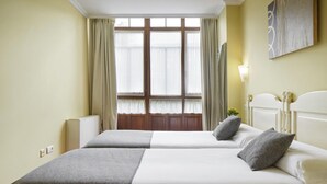 A hotel room with two beds, a large window with curtains, a radiator, and a painting on the wall. - Iraipe Ongi Hotel (Oñati)